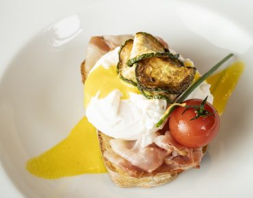 piatto con pane, uovo alla benedicte, prosciutto, pomodoro e zucchine